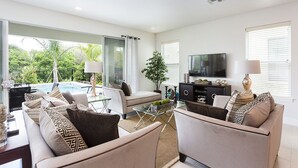 A modern living room with a sofa, armchairs, a coffee table, a TV, and a view of a swimming pool.