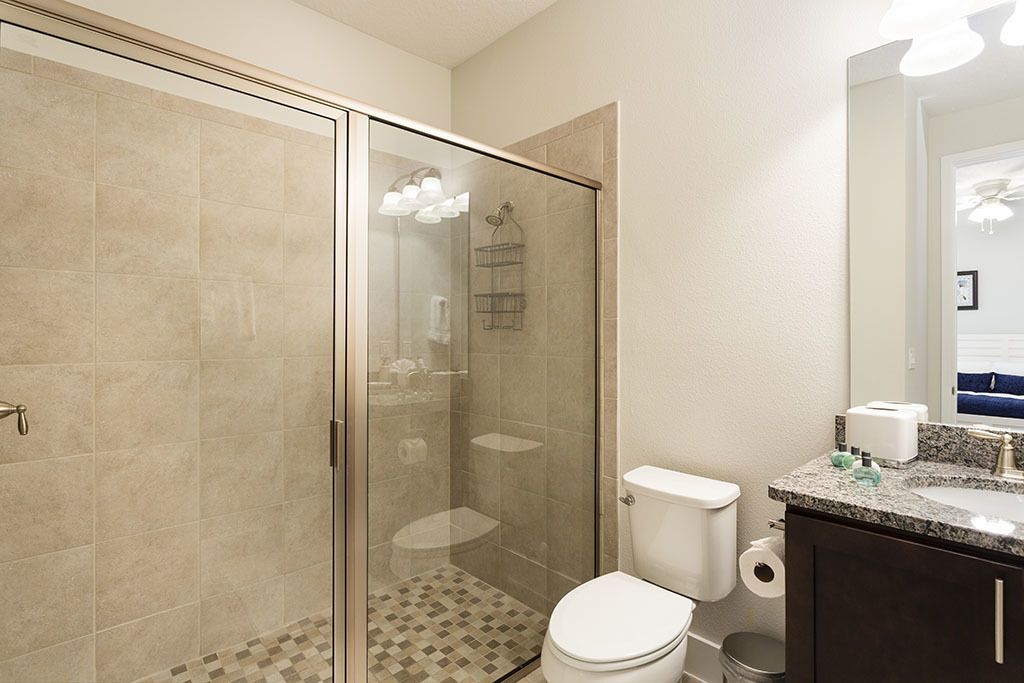 A bathroom with a glass-enclosed shower, a toilet, a sink with a granite countertop, and a mirror.