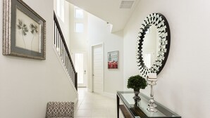A hallway with a staircase, a bench, a glass-top console table, a decorative mirror, and a framed artwork on the wall.