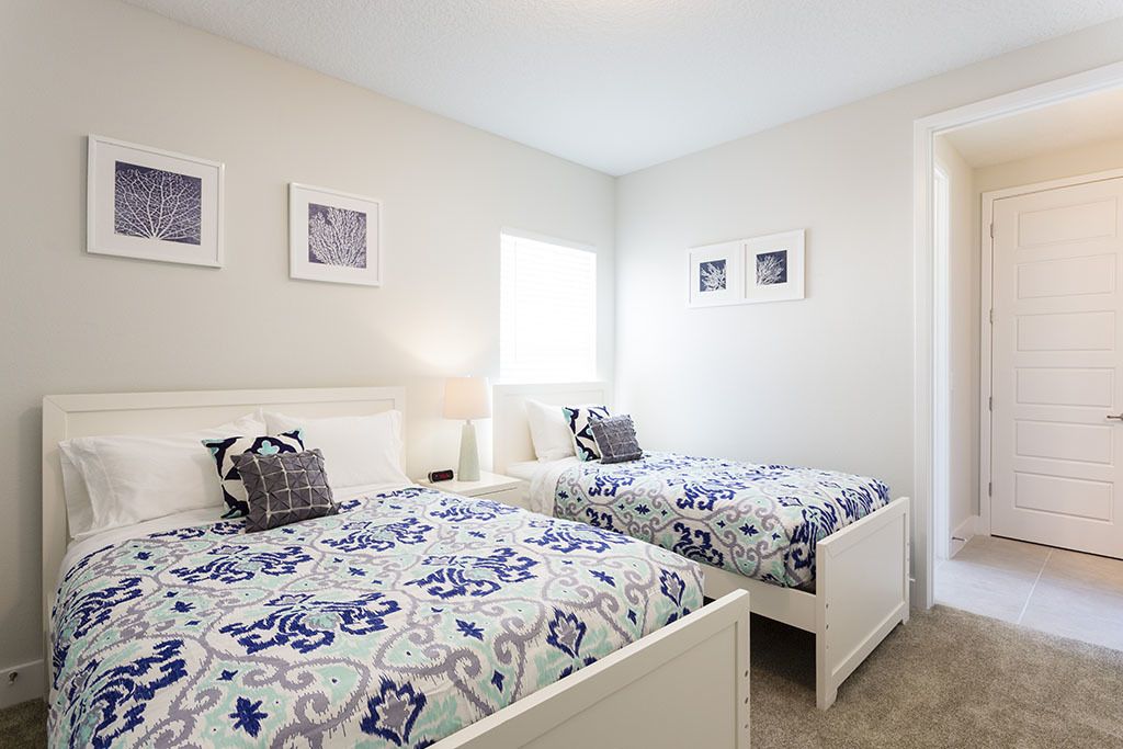 A bedroom with two beds, a nightstand, a lamp, and framed artwork on the wall.