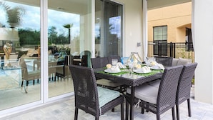 A dining area with a glass table, wicker chairs, and a view of the garden through the glass doors.