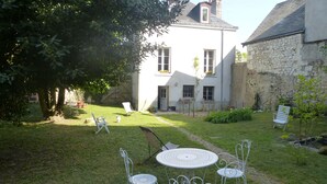 A courtyard with a white metal table and chairs, a stone building, and a tree providing shade. - La Petite Vigne (Amboise)