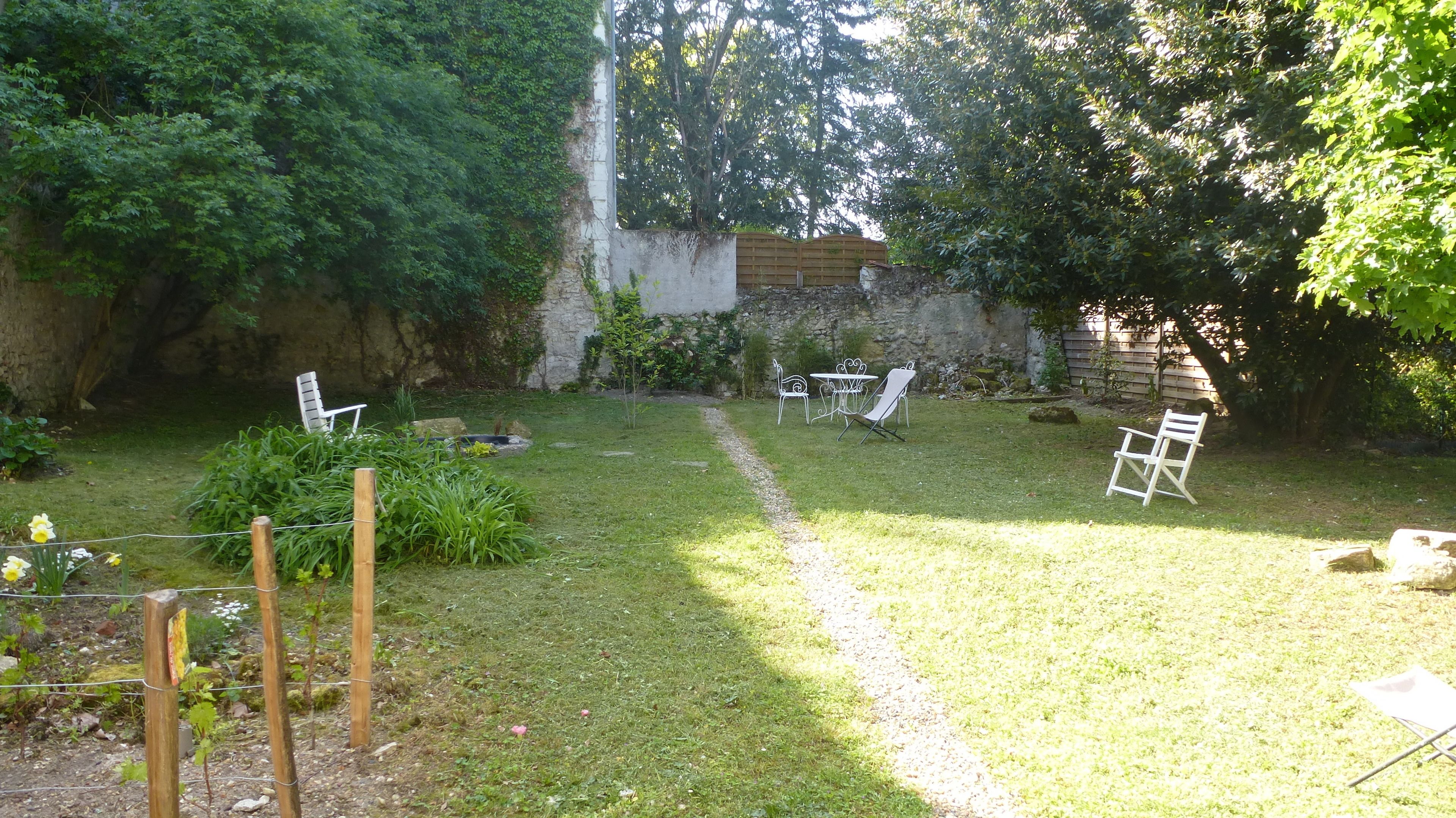 A garden with a stone wall, a small pond, and white metal chairs and tables.