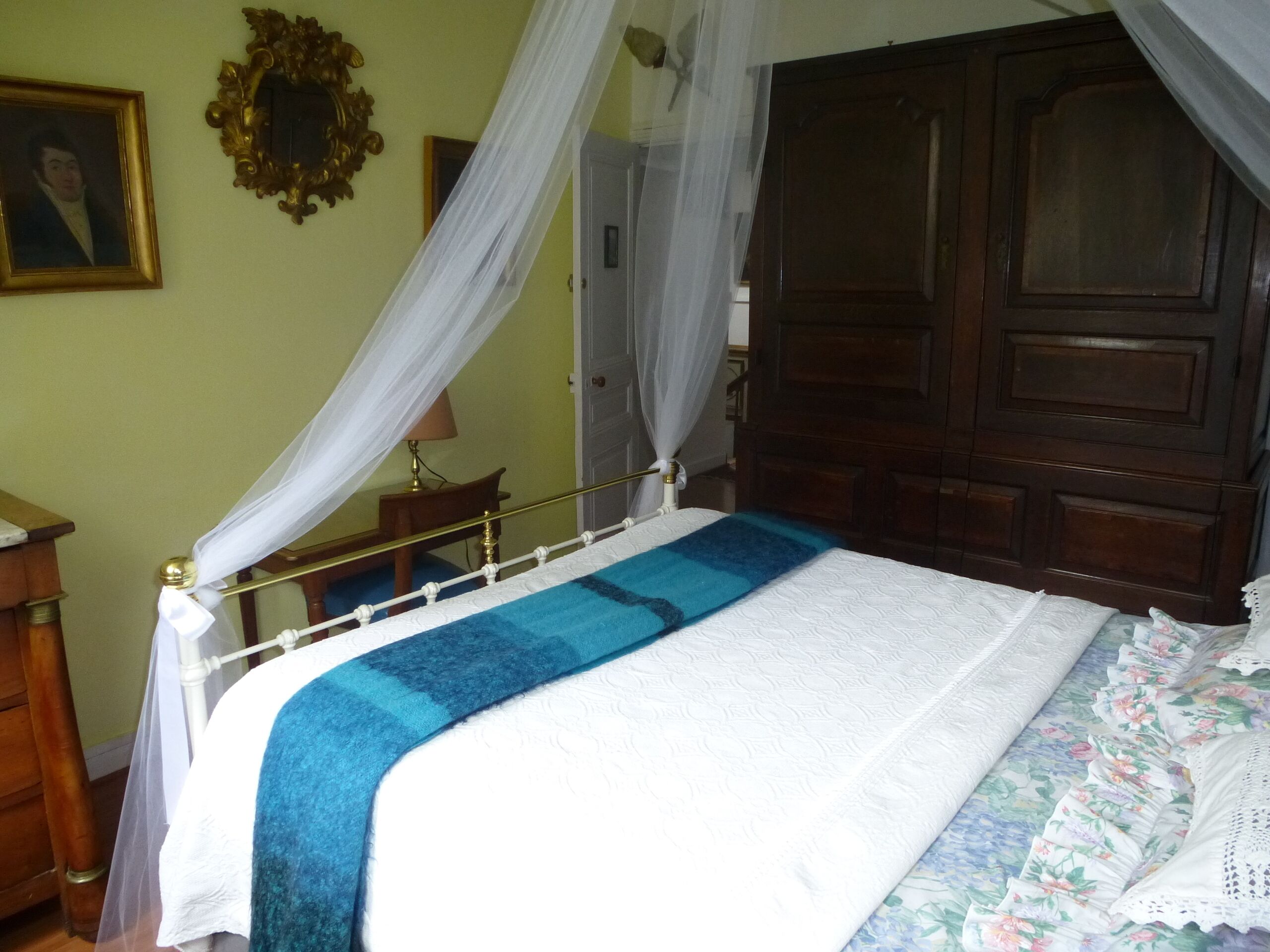 A bedroom with a bed, a wooden wardrobe, a nightstand, and a mirror on the wall.