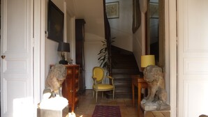A room with a staircase, a wooden cabinet, a chair, and two lion statues. - La Petite Vigne (Amboise)