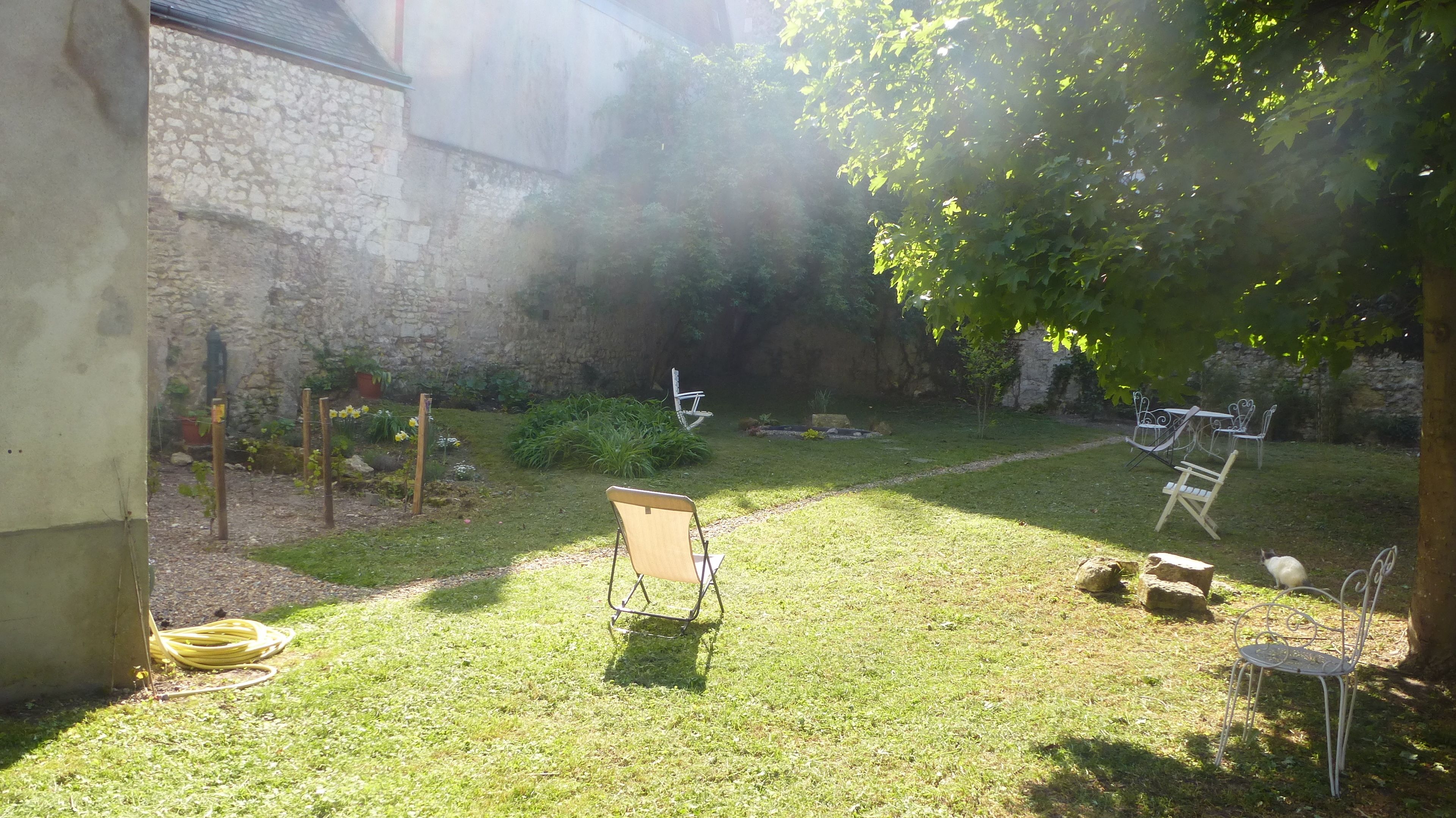 A grassy outdoor area with a stone wall, a metal chair, and a table with chairs.