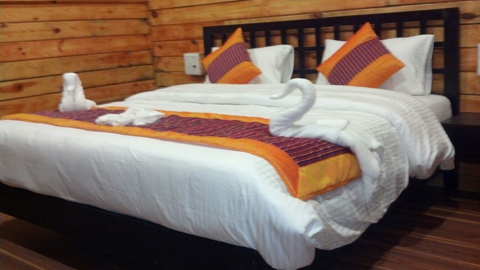 A wooden cabin-style room with a bed featuring white bedding and orange accents.