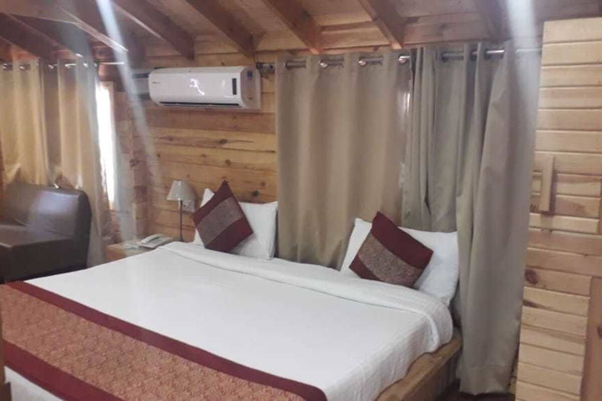 A wooden cabin room with a bed, curtains, a chair, and an air conditioning unit.