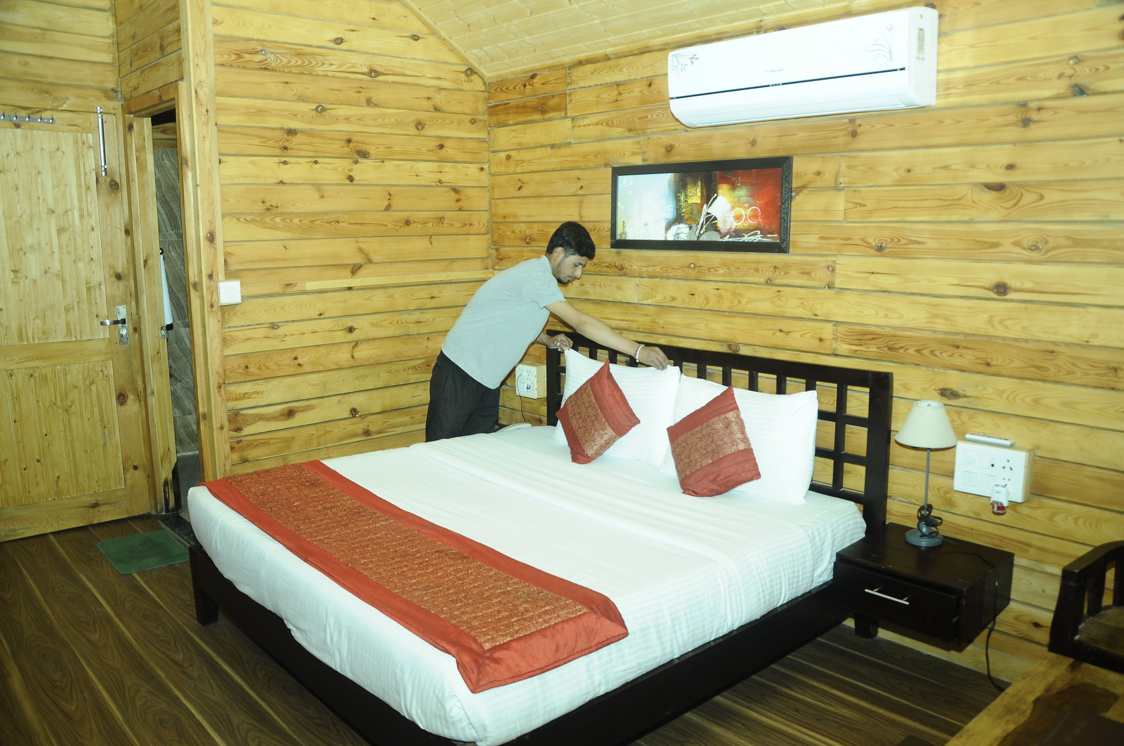 Habitación de cabaña de madera con una cama, una mesita de noche, una lámpara y un equipo de aire acondicionado.