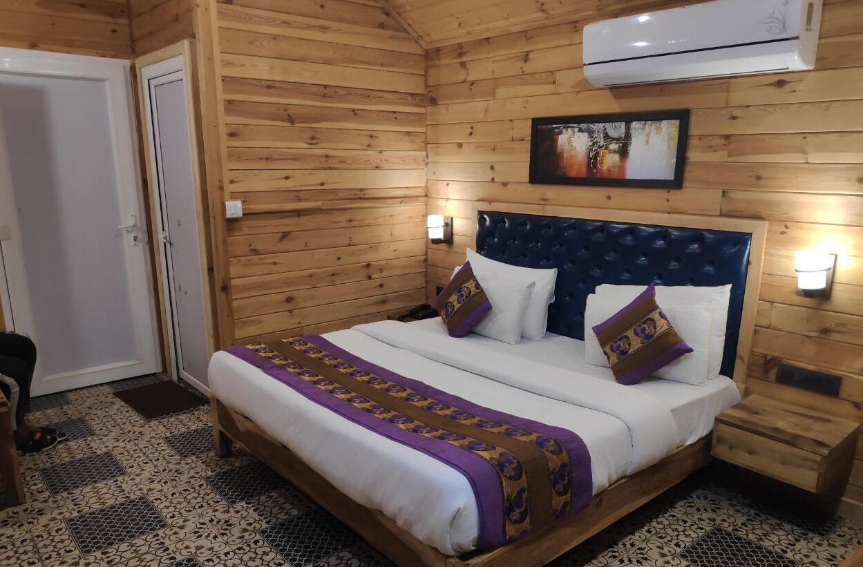 A wooden-paneled room with a bed, two bedside tables, an air conditioning unit, and a wall-mounted picture.