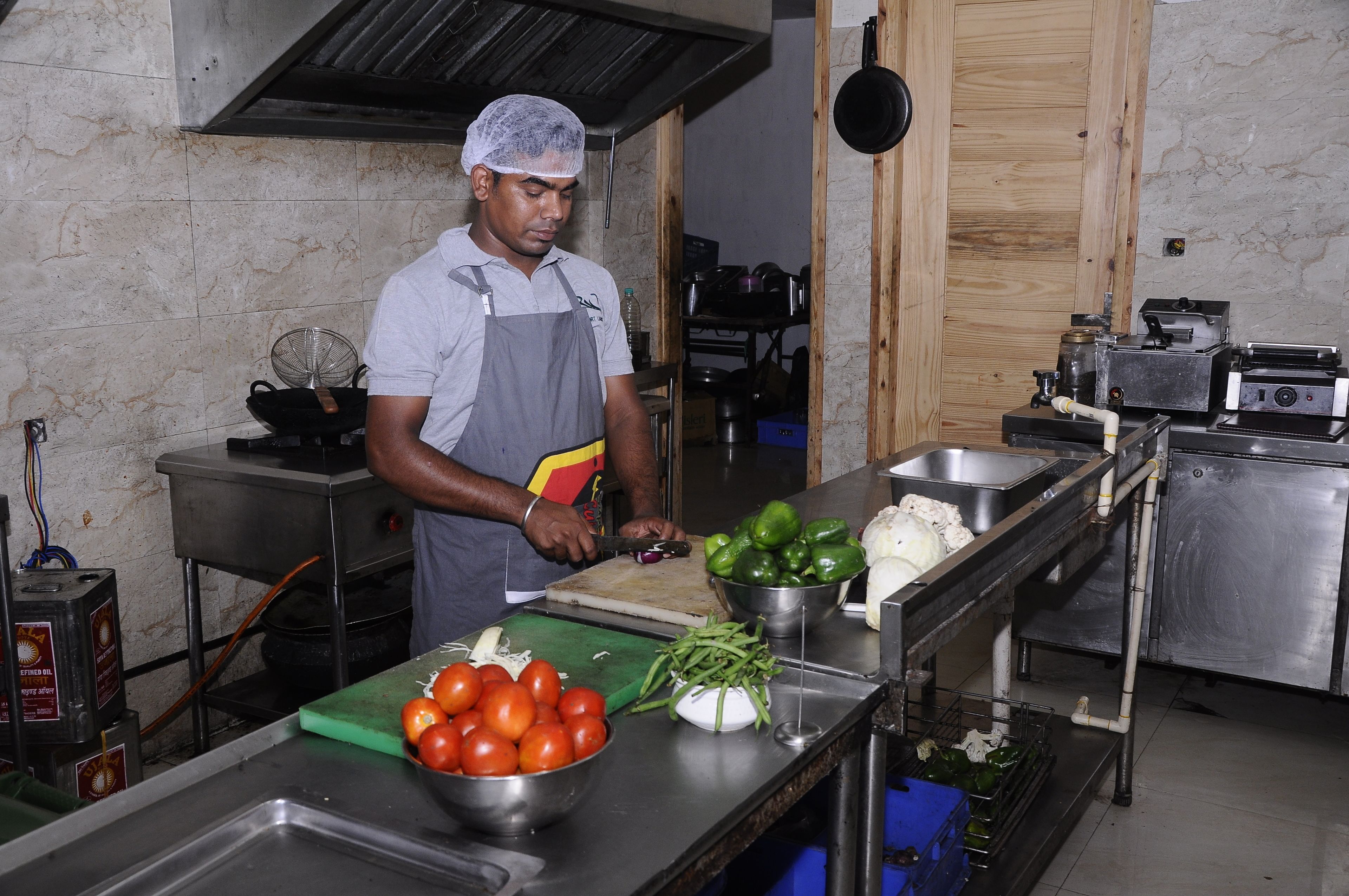 Una cocina con electrodomésticos de acero inoxidable, una tabla de cortar con verduras y una persona preparando comida.