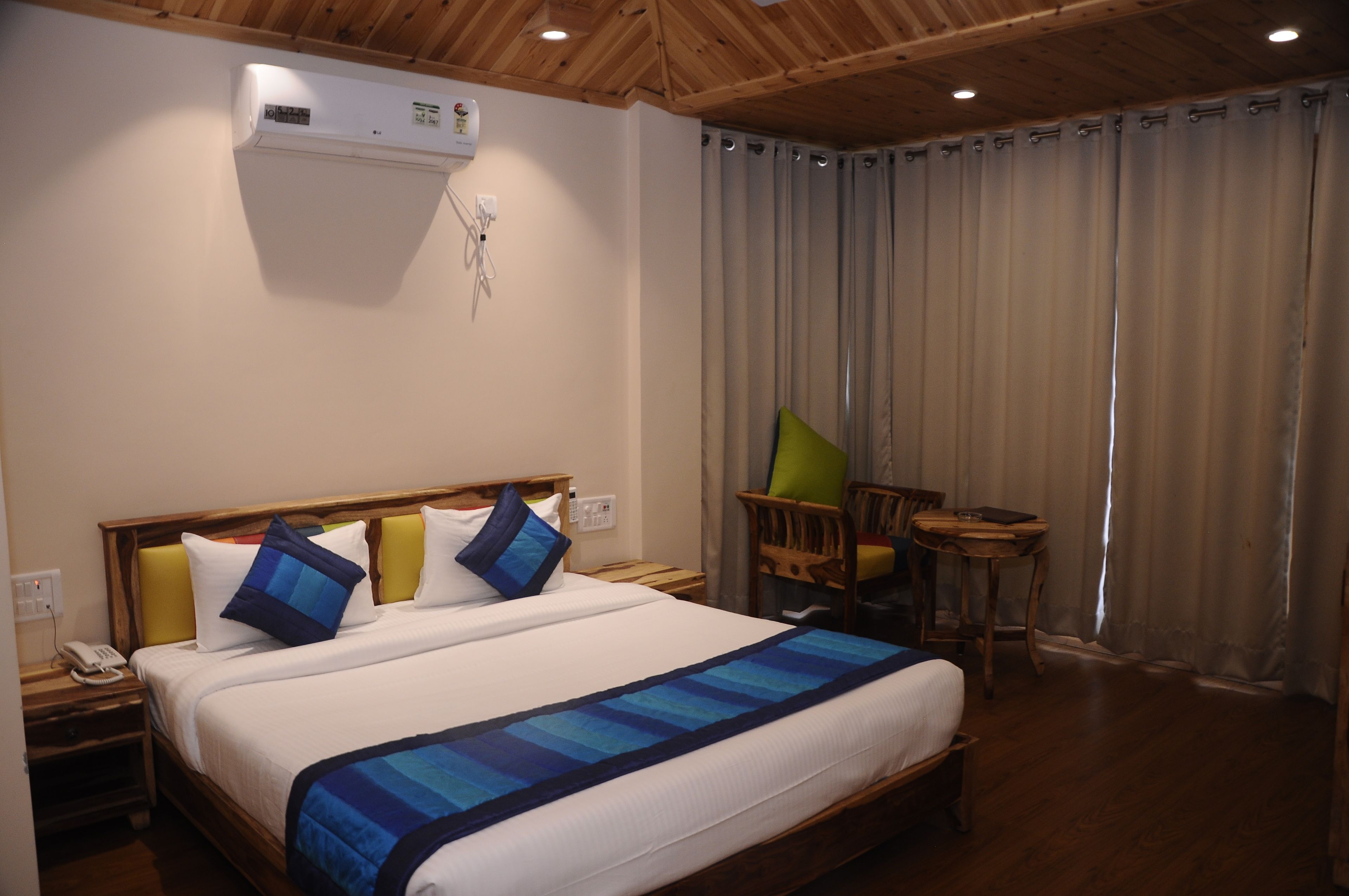 A hotel room with a wooden ceiling, a bed with blue and white bedding, a small table, and a chair.