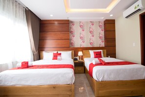 Ett hotellrum med två sängar i trä, vita sängkläder, röda detaljer, en blommig tapet och en luftkonditioneringsanläggning.