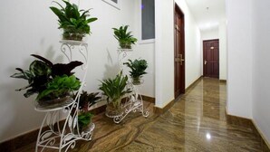 A hallway with marble flooring and white walls. There are three white metal stands with potted plants. A wooden door is visible in the background. - RedDoorz Plus near Tan Son Nhat Airport 2 (Ho Chi Minh City)