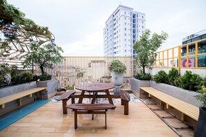 An outdoor patio with a wooden table and benches, surrounded by potted plants and a metal fence.