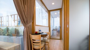 A room with a wooden table, chairs, a bench, a glass door leading outside, and a view of greenery. - RedDoorz Plus near Saigon Train Station (Ho Chi Minh City)