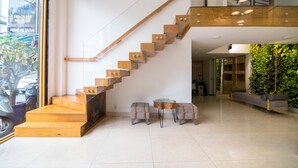 A modern hotel interior with a wooden staircase, a seating area with two ottomans, and a green wall. - RedDoorz Plus near Saigon Train Station (Ho Chi Minh City)