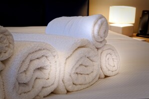 A neatly made bed with rolled white towels and a bedside lamp. - Albergo Giuan Arma di Taggia (Arma di Taggia)