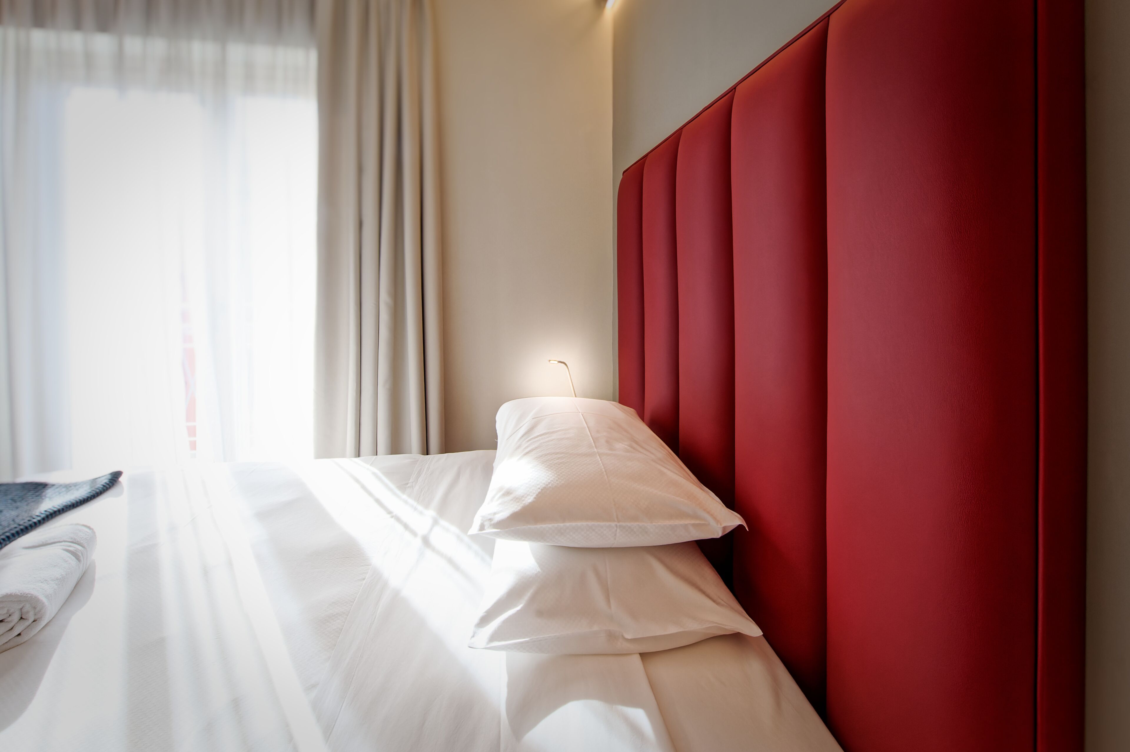 Ein Hotelzimmer mit einem Bett, einem roten Kopfteil und einem Fenster mit Vorhängen.