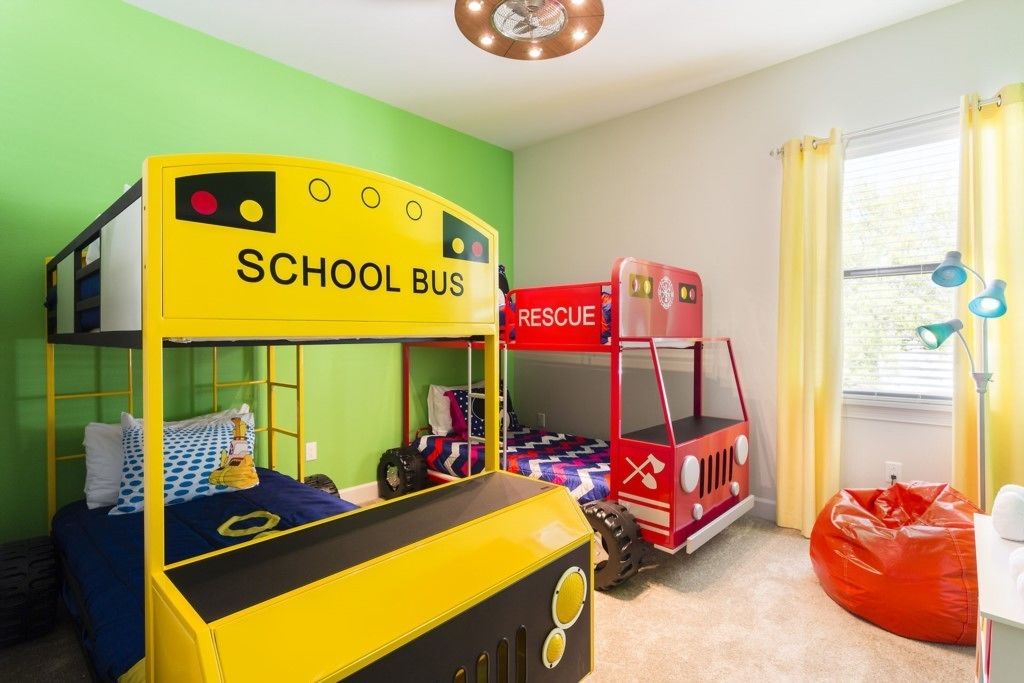 Une chambre d’enfant avec des lits superposés, un lit en forme de bus scolaire, un lit en forme de véhicule de secours rouge et un fauteuil en forme de sac à haricots.