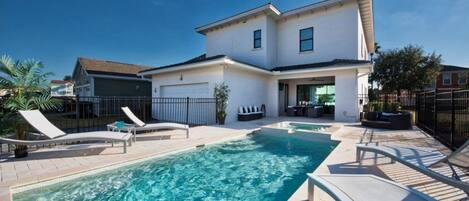 A two-story house with a swimming pool, outdoor seating, and a garage.