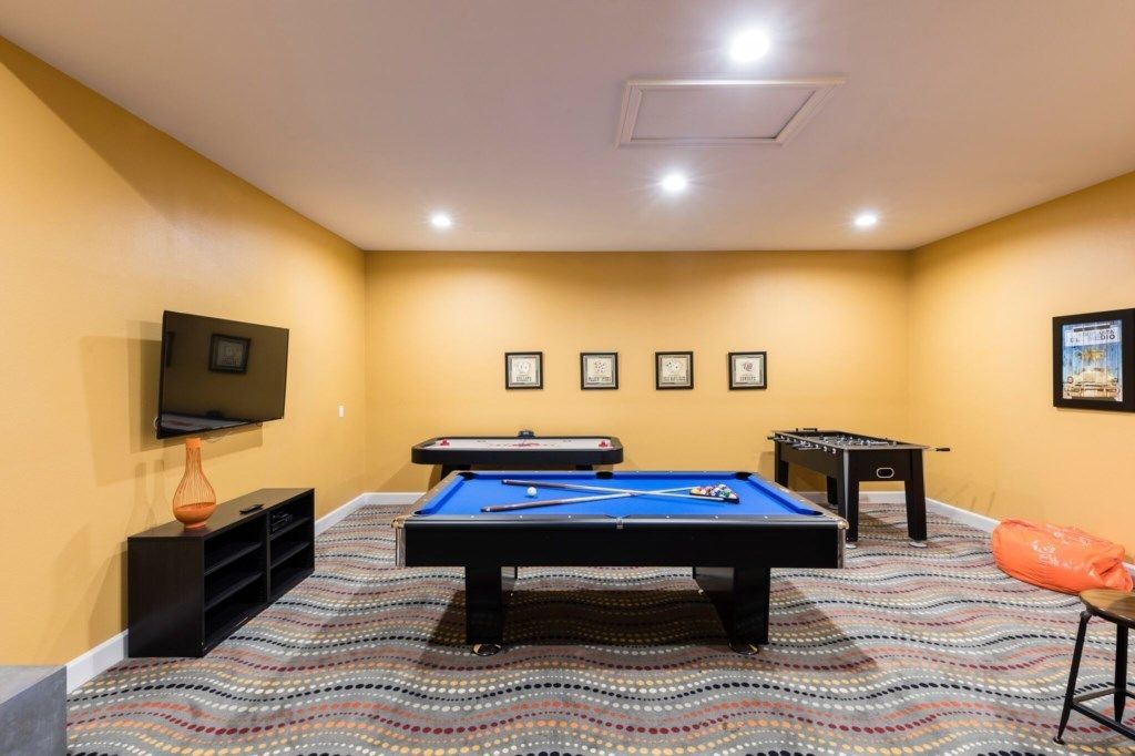 A pool table with billiard balls, a foosball table, and a television mounted on the wall.