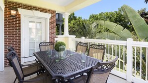Eine Terrasse mit Tisch und Stühlen, ein weißer Zaun und eine Ziegelwand.