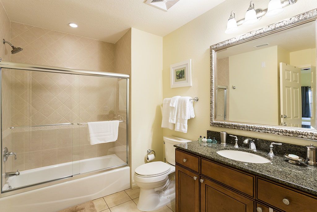 A bathroom with a glass-enclosed shower, a toilet, a sink with a vanity, and a large mirror.