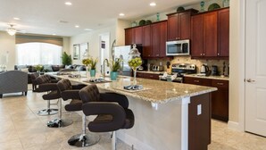 A modern kitchen with dark wooden cabinets, a granite countertop, and stainless steel appliances. There are bar stools and a large island with a glass top. - Je62429 - Reunion Resort - 8 Bed 8 Baths Villa (Kissimmee)