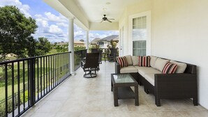 A covered balcony with a sofa, chairs, and a table.