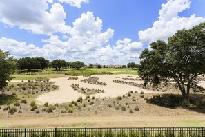 Een golfbaan met zandbunkers, bomen en een heldere lucht.