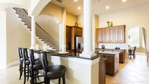 A spacious kitchen with a central island, dark wooden chairs, and a staircase leading to another level.