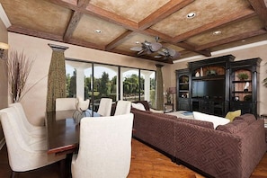 Relax in this spacious living area with a high ceiling, featuring a large sectional sofa, dining table, and television.