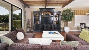 Een moderne woonkamer met een grote televisie, donker houten kasten en een plafondventilator.