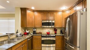 Una cocina con armarios de madera, electrodomésticos de acero inoxidable, encimeras de granito y un lavamanos doble.