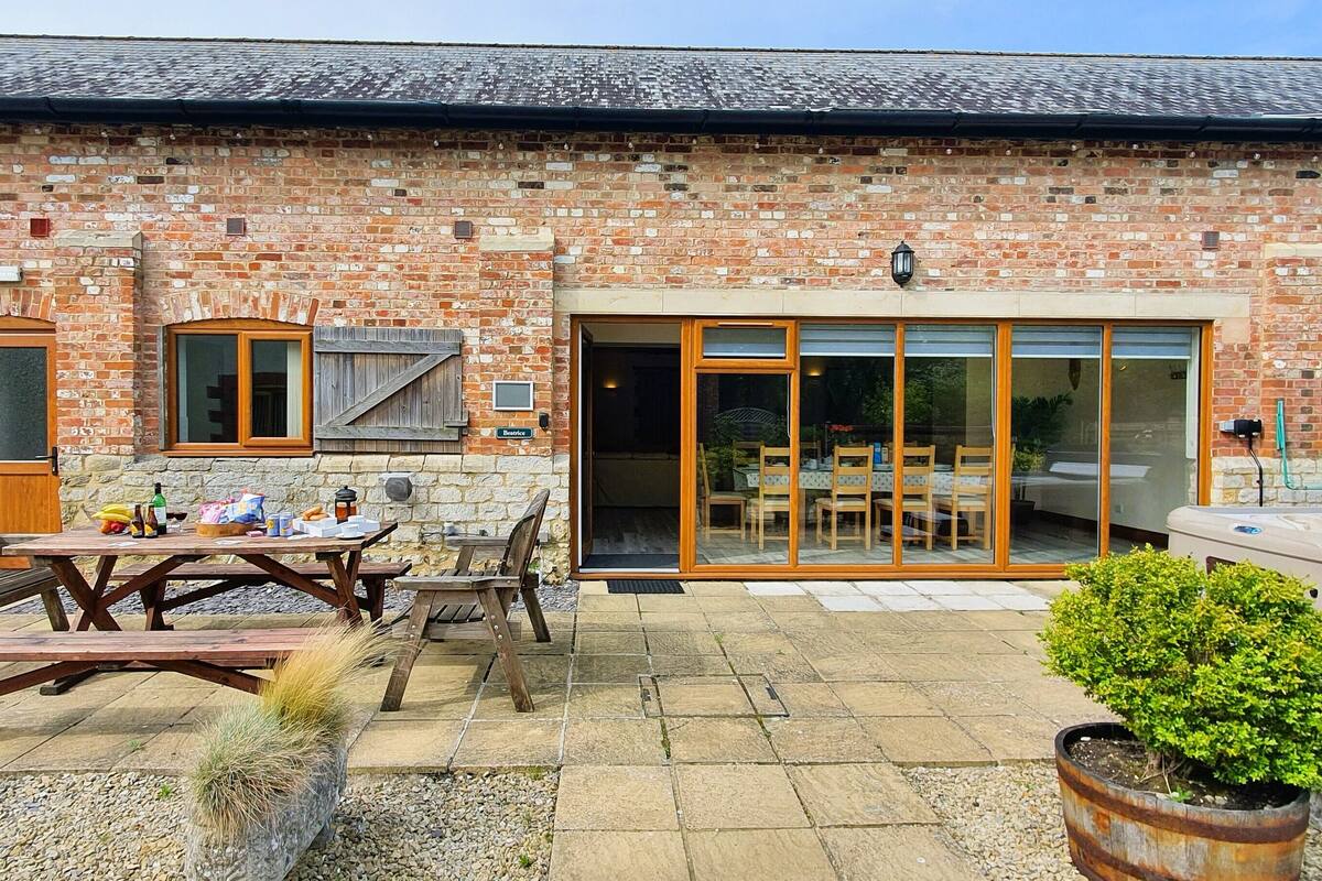 A brick building with a patio area featuring picnic tables, benches, and a hot tub.
