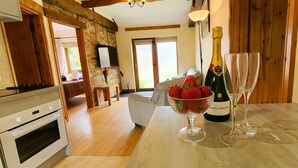 A kitchen with a wooden table, a bottle of champagne, two wine glasses, and a bowl of strawberries. - The Victorian Barn self catering holidays with pool & hot tubs (Blandford Forum)