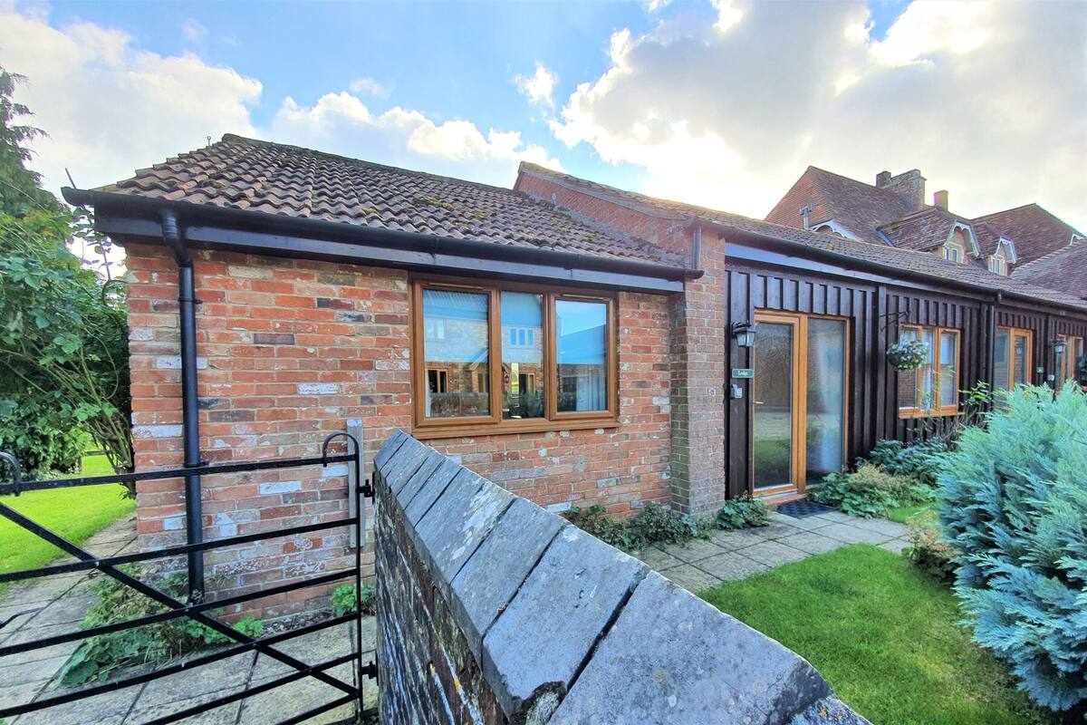 A brick house with a tiled roof, wooden-framed windows, and a stone wall.