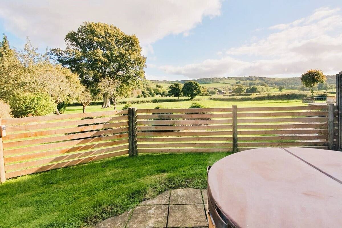 A patio area with a wooden fence, a stone table, and a view of a green landscape with trees and hills.
