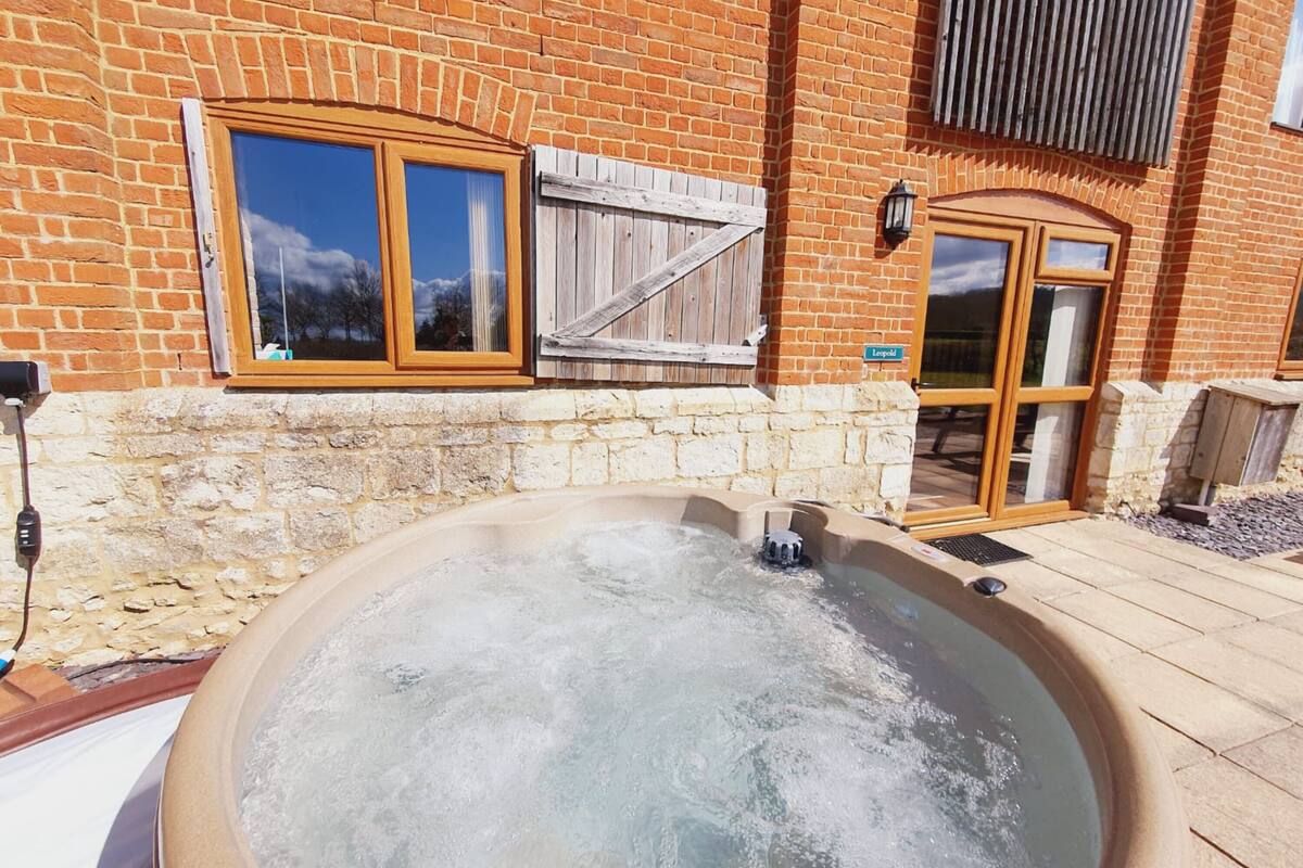 A hot tub in front of a brick building with a stone wall and wooden shutters.