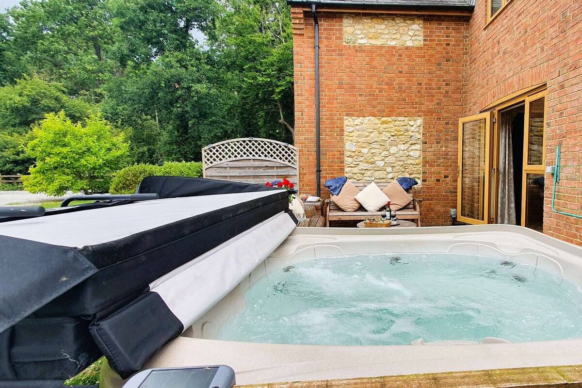 A hot tub in a backyard with a brick wall, a wooden deck, and a covered seating area.