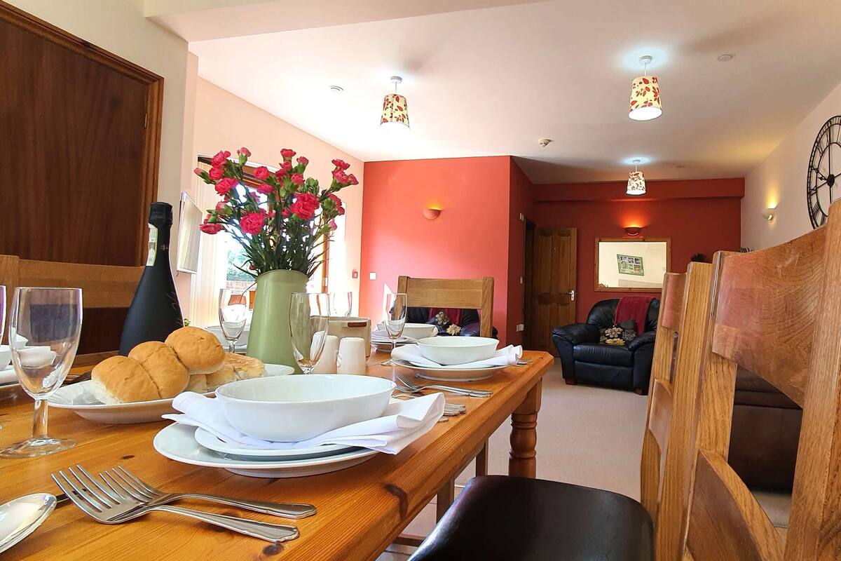 A dining area with a wooden table set for a meal, a vase with flowers, and a clock on the wall.
