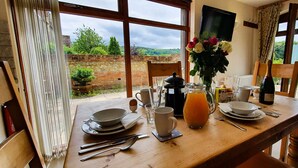 A breakfast table set with plates, bowls, cups, and a pitcher of orange juice, with a view of greenery outside. - The Victorian Barn self catering holidays with pool & hot tubs (Blandford Forum)