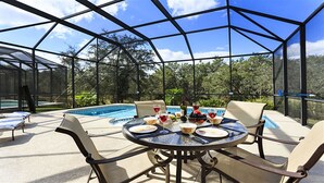 An outdoor patio with a pool, round table, chairs, and a glass enclosure. - Je47048 - Reunion Resort - 4 Bed 4 Baths Villa (Kissimmee)