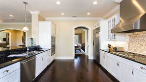 A modern kitchen with dark wood flooring, white cabinetry, stainless steel appliances, and a central island.