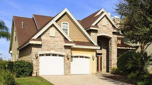 Une maison à deux étages avec une façade en pierre, deux portes de garage et un jardin aménagé à l’avant.