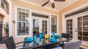 Une terrasse couverte avec une table à plateau de verre, des chaises en osier et un ventilateur de plafond.