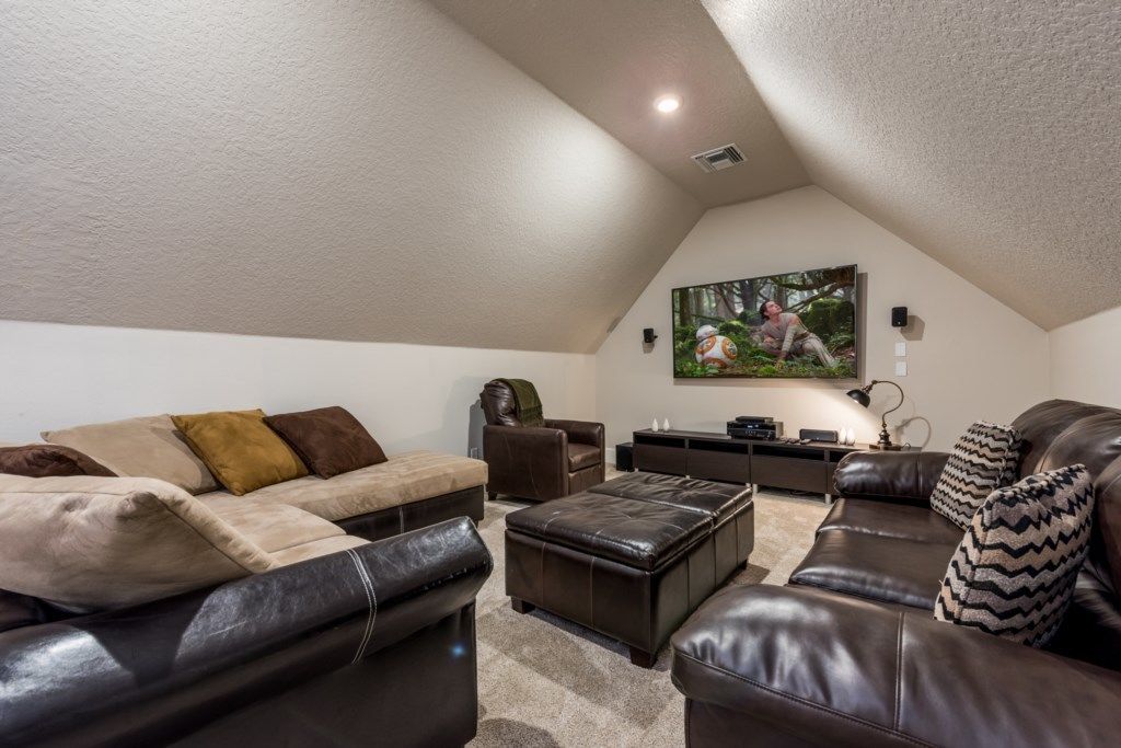 A cozy living room with a high ceiling, a large flat-screen TV mounted on the wall, and a comfortable seating area with leather sofas and ottomans.