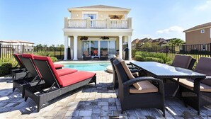 A two-story house with a balcony, a pool, outdoor furniture, and a patio area.