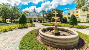 A courtyard with a central fountain, surrounded by well-manicured hedges and a paved walkway.